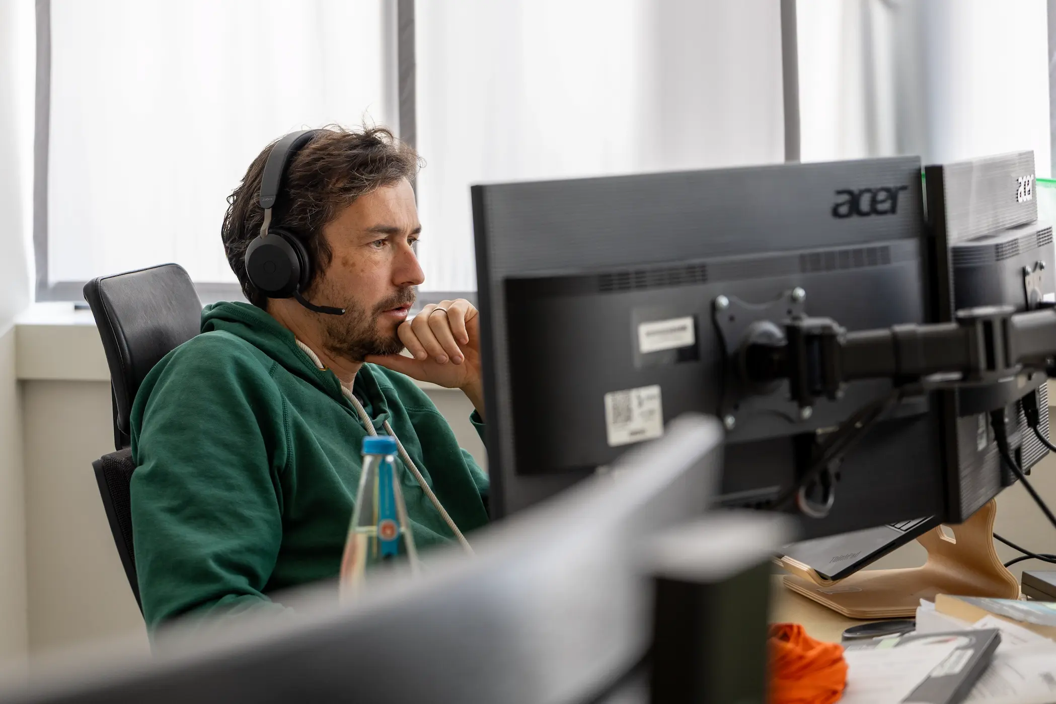 Mann mit Headset arbeitet konzentriert an zwei Monitoren.